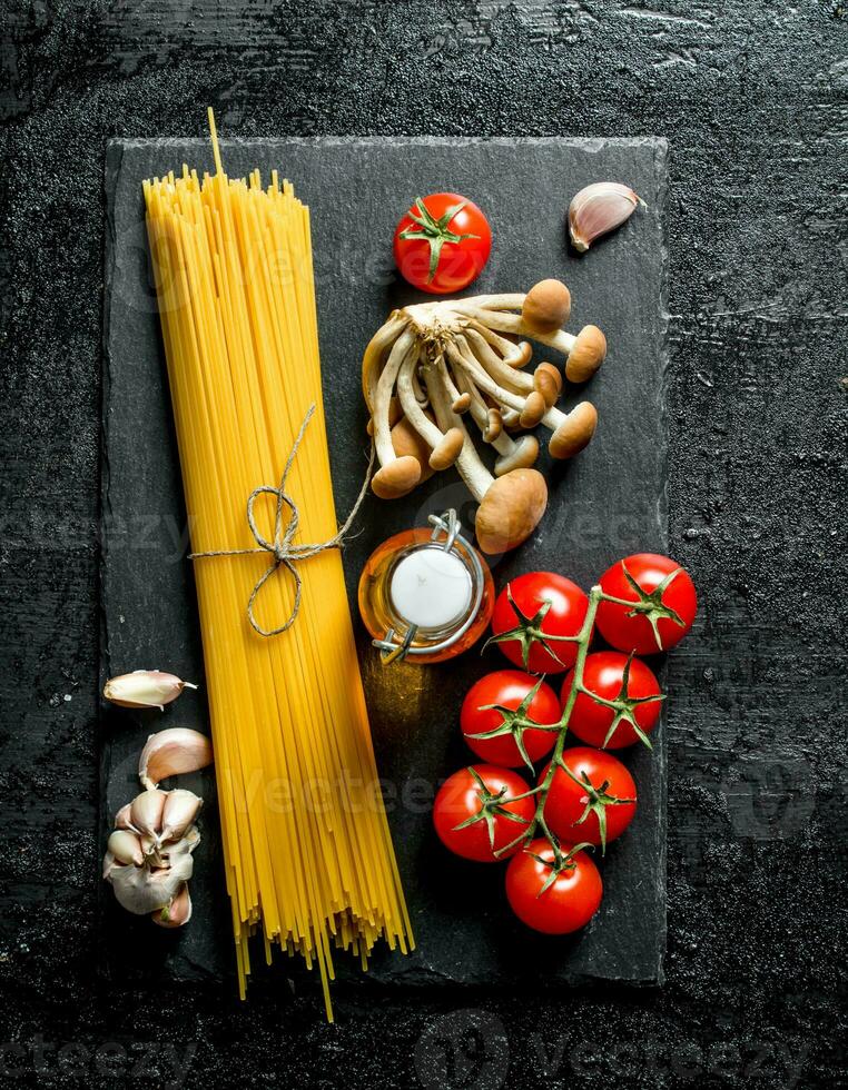 Raw spaghetti on black stone Board with tomatoes, garlic, mushrooms and oil. photo