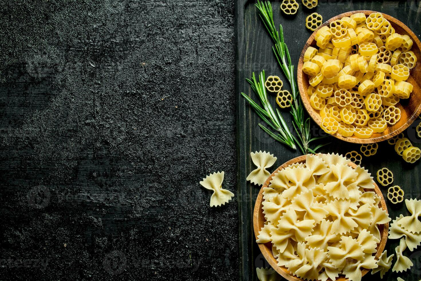 Different types of raw pasta in bowls with the rosemary. photo