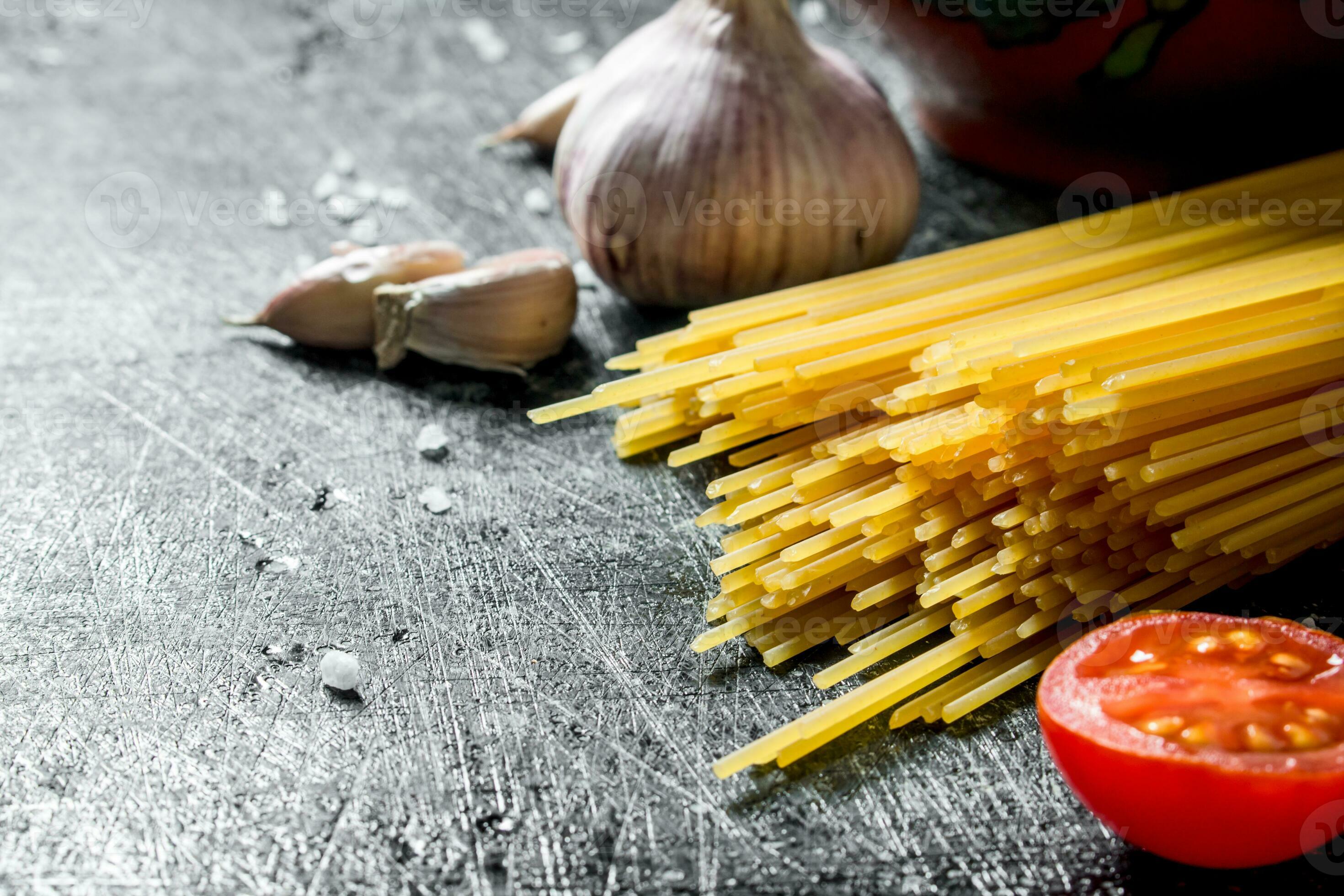 Raw spaghetti with garlic cloves and tomato. 32016867 Stock Photo at Vecteezy