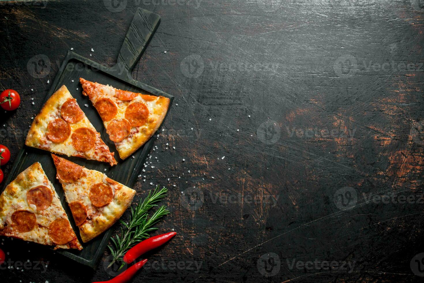 Slices of pepperoni pizza with chili, rosemary and cherry tomatoes. photo