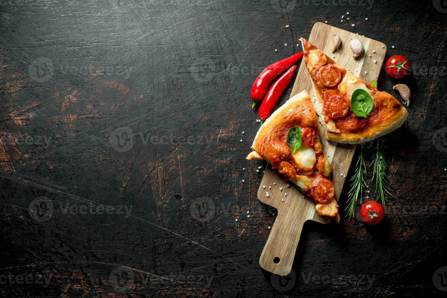 Slices of homemade pizza on a cutting Board with chili, tomatoes and rosemary. photo