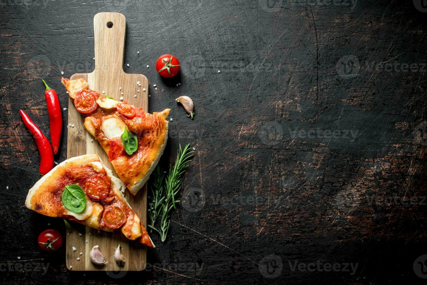 Slices of homemade pizza on a cutting Board with chili, tomatoes and rosemary. photo