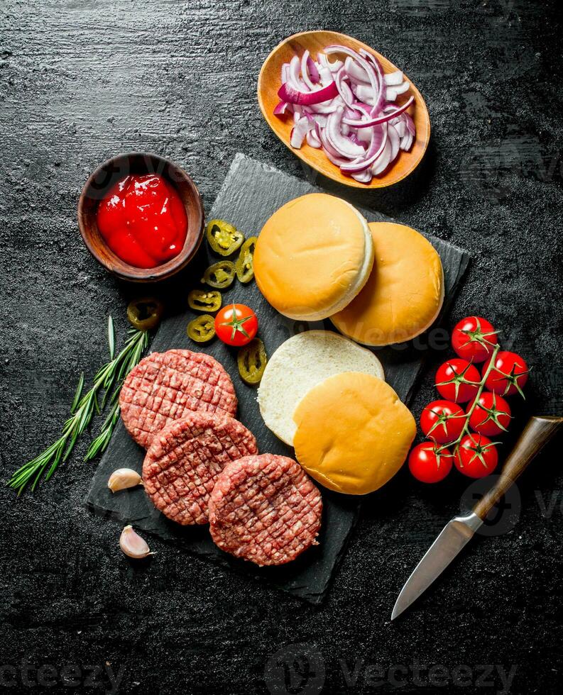 Raw burgers with tomatoes, scones, sauce and chopped onion. photo
