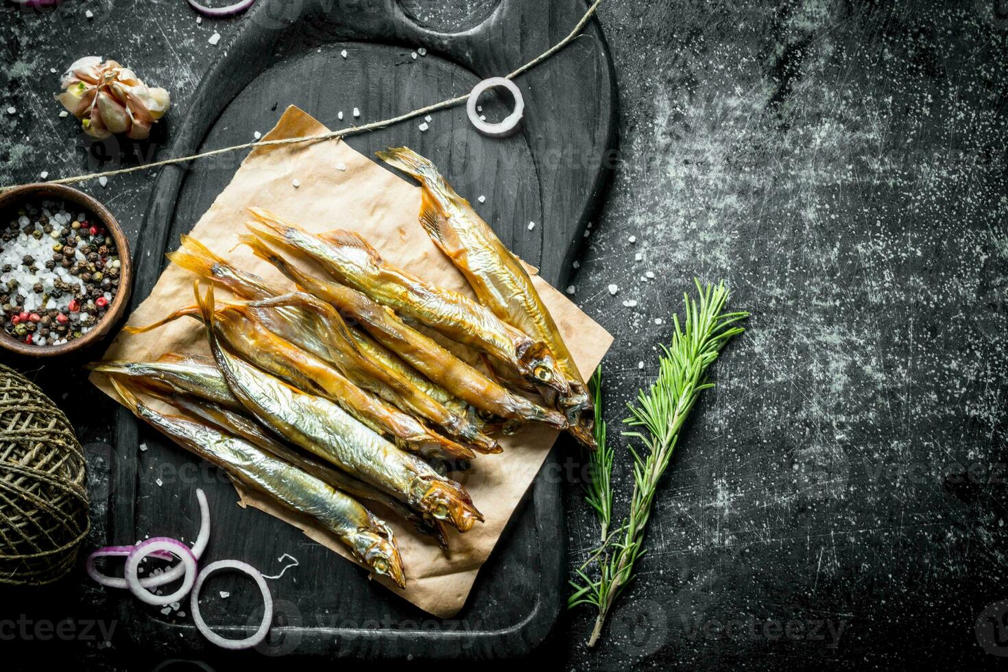 Smoked fish on a cutting Board with rosemary, twine, spices and garlic cloves. photo