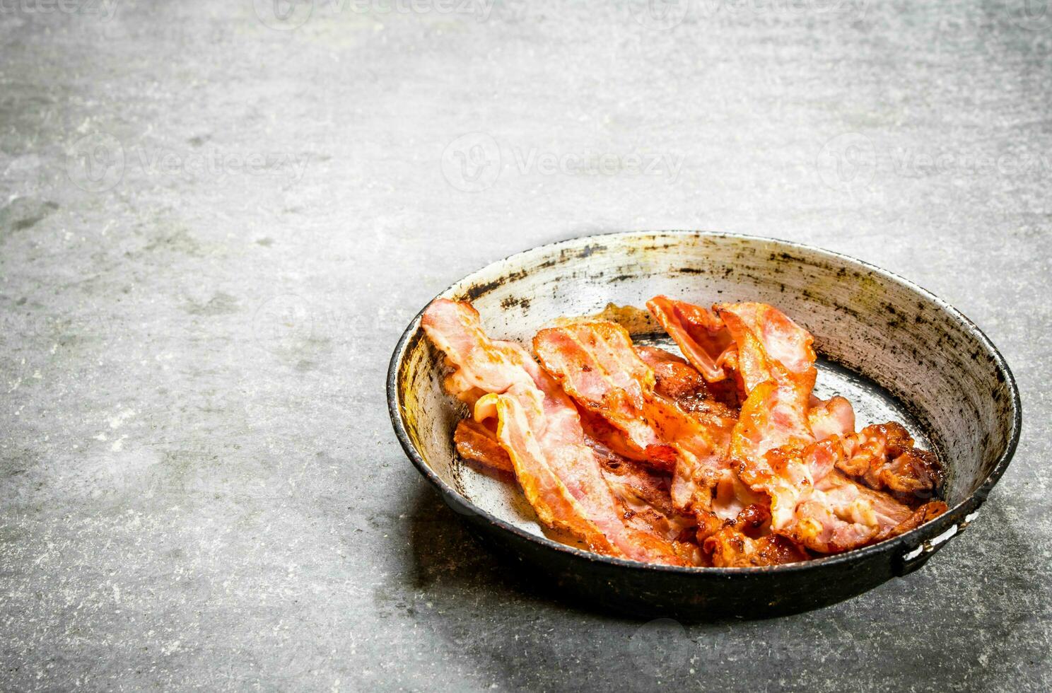 Fried bacon in a frying pan. On stone background. photo