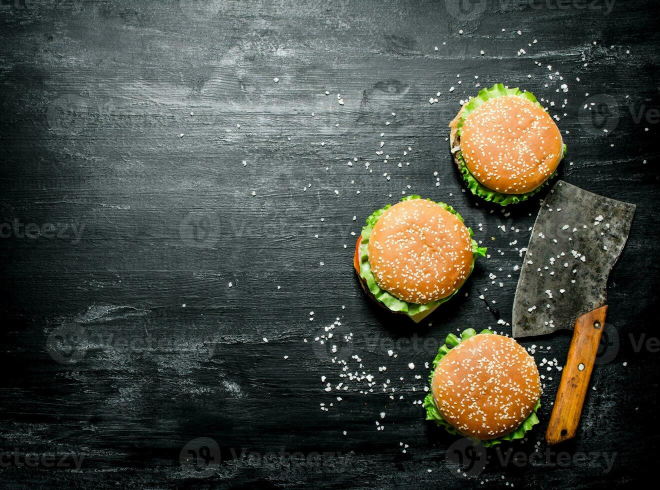 Three burgers with a meat ax. On black chalkboard. photo