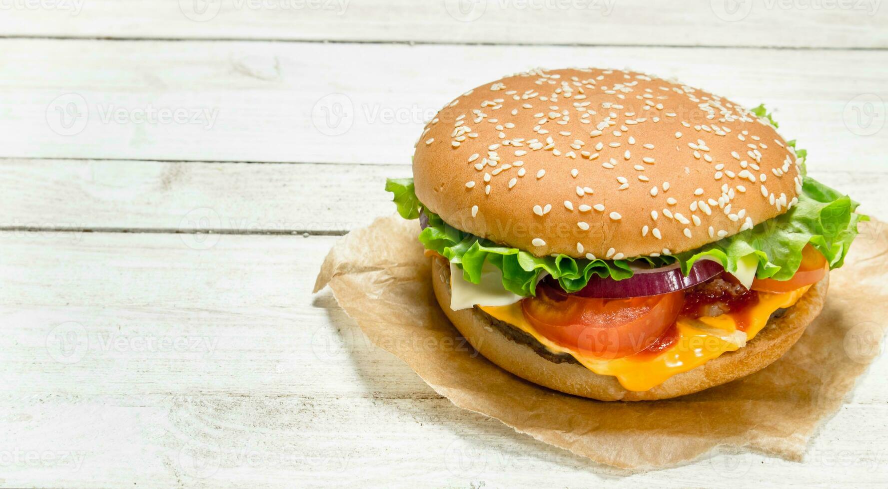 Burger with beef, cheese and vegetables on paper. photo