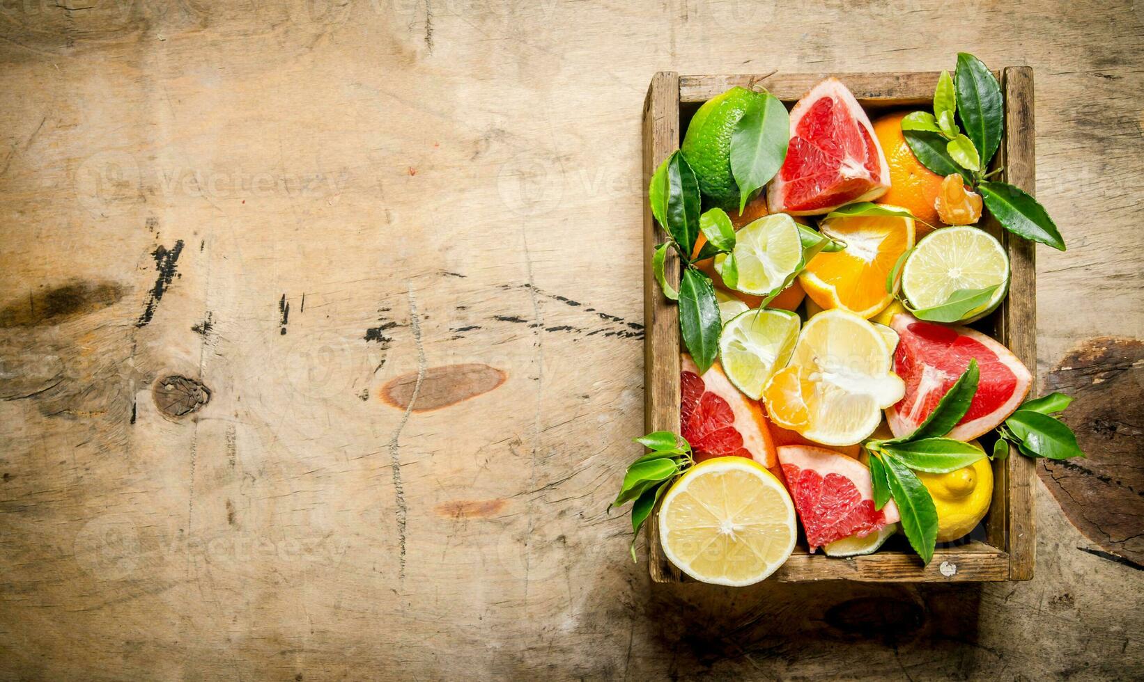 A box of citrus fruit - grapefruit, orange, tangerine, lemon, lime and leaves . photo