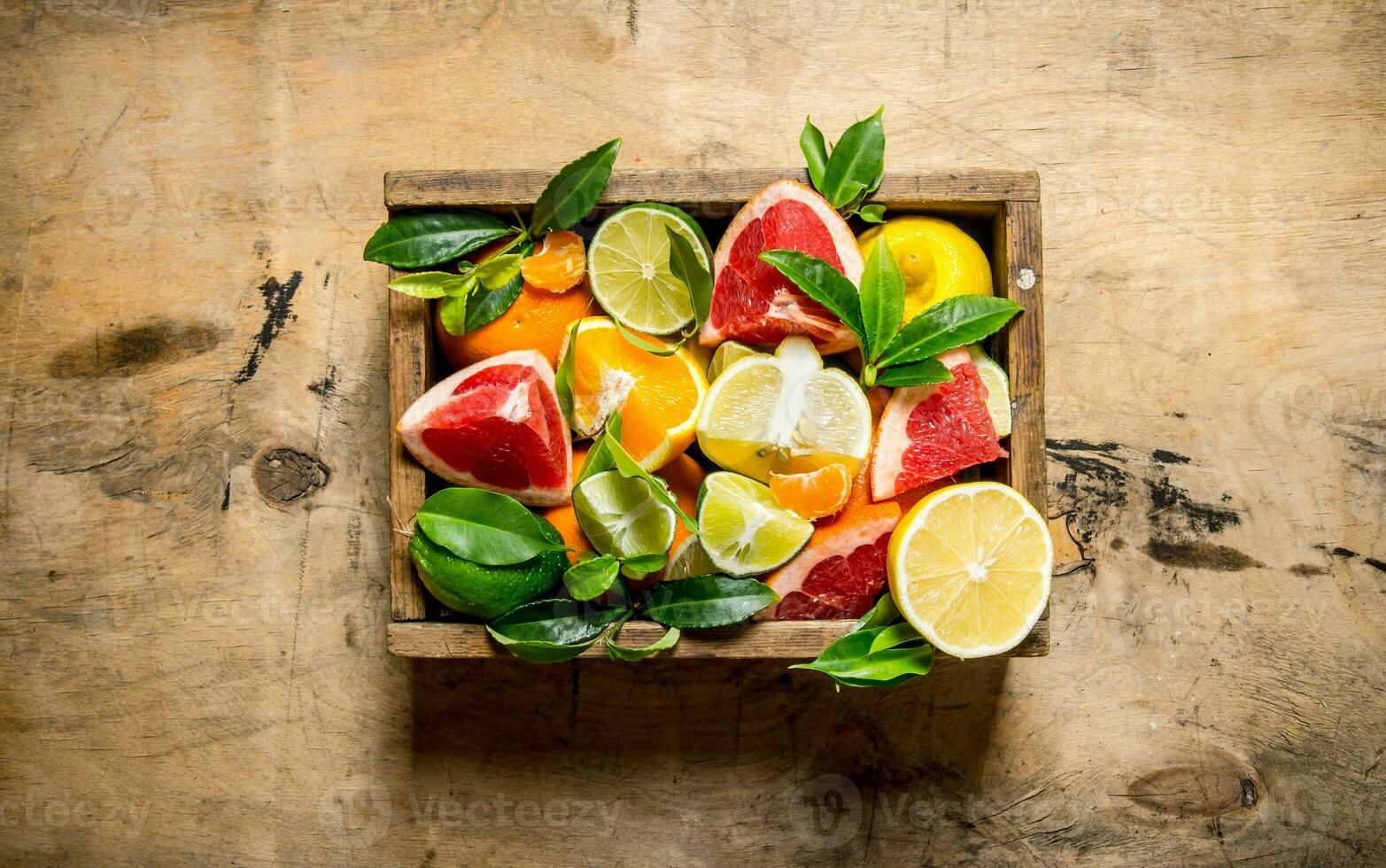 A box of citrus fruit - grapefruit, orange, tangerine, lemon, lime and leaves . photo