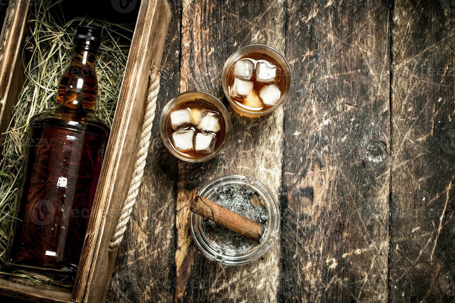 Whiskey background. A bottle of whiskey in an old box with glasses and a cigar. photo