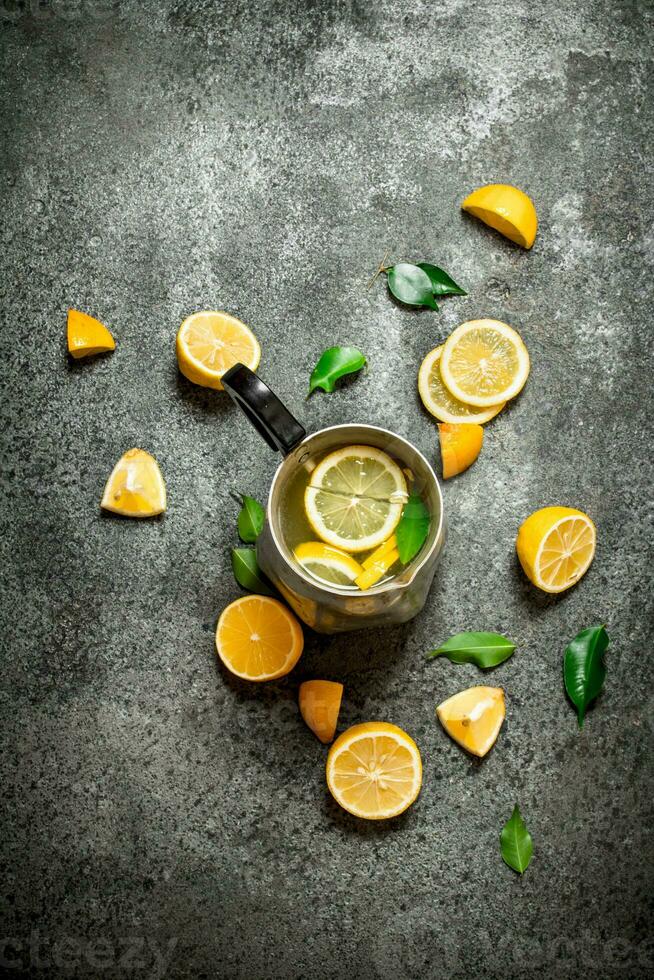 Cold lemonade in a jug with slices of lemon and green leaves. photo