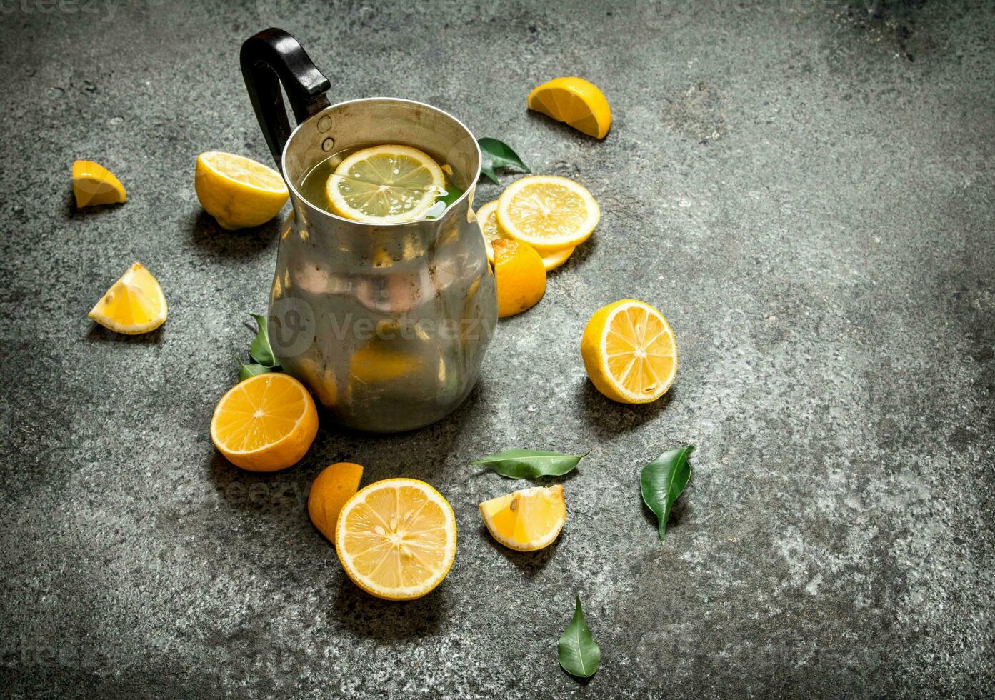 Cold lemonade in a jug with slices of lemon and green leaves. photo