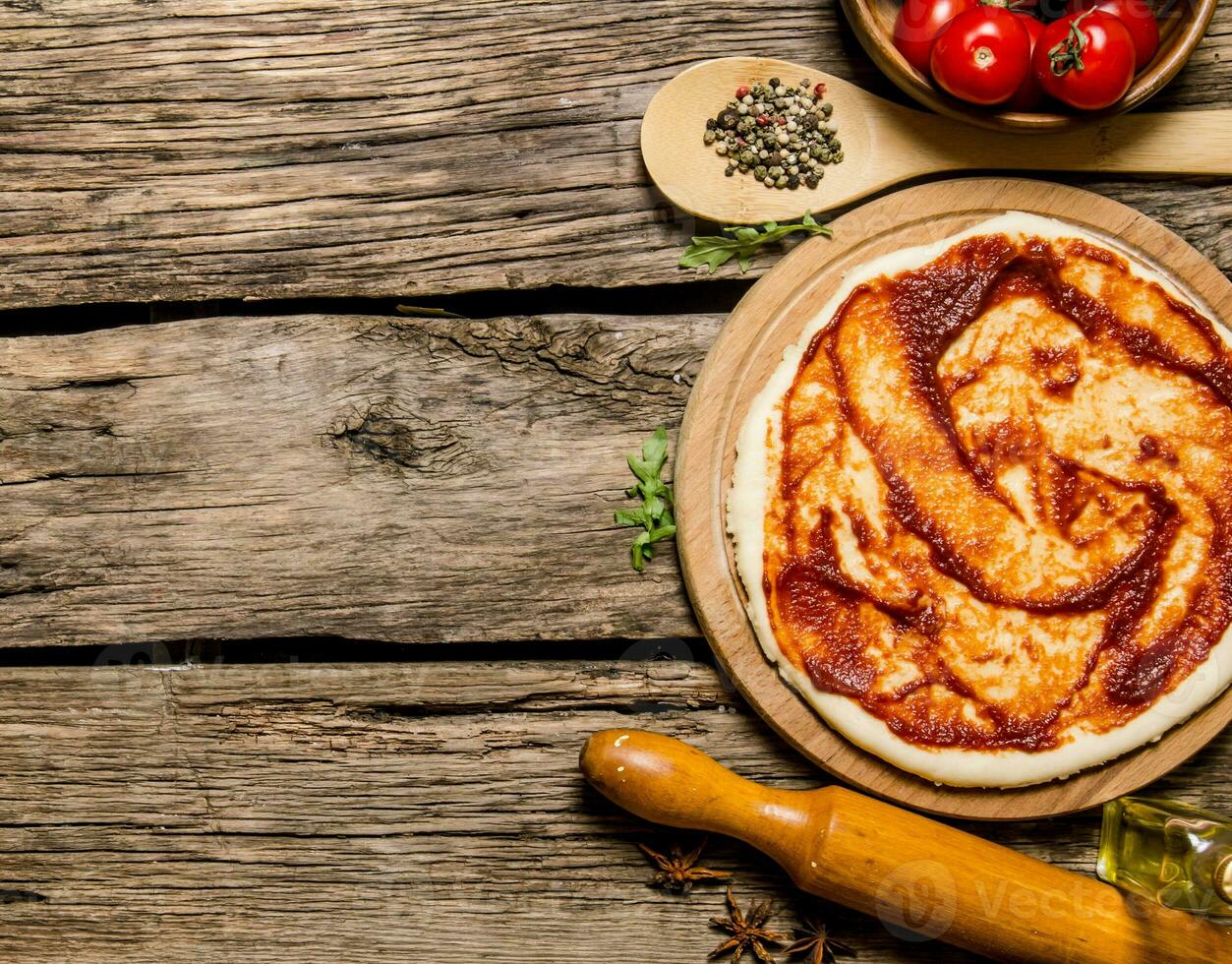 The rolled out pizza dough with tomato sauce, rolling pin and spices. photo