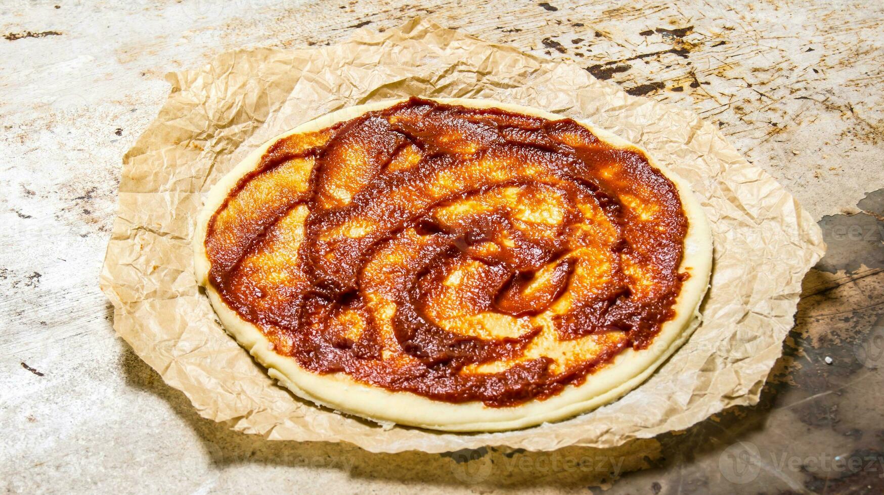 The rolled out pizza dough with tomato paste on old paper. photo