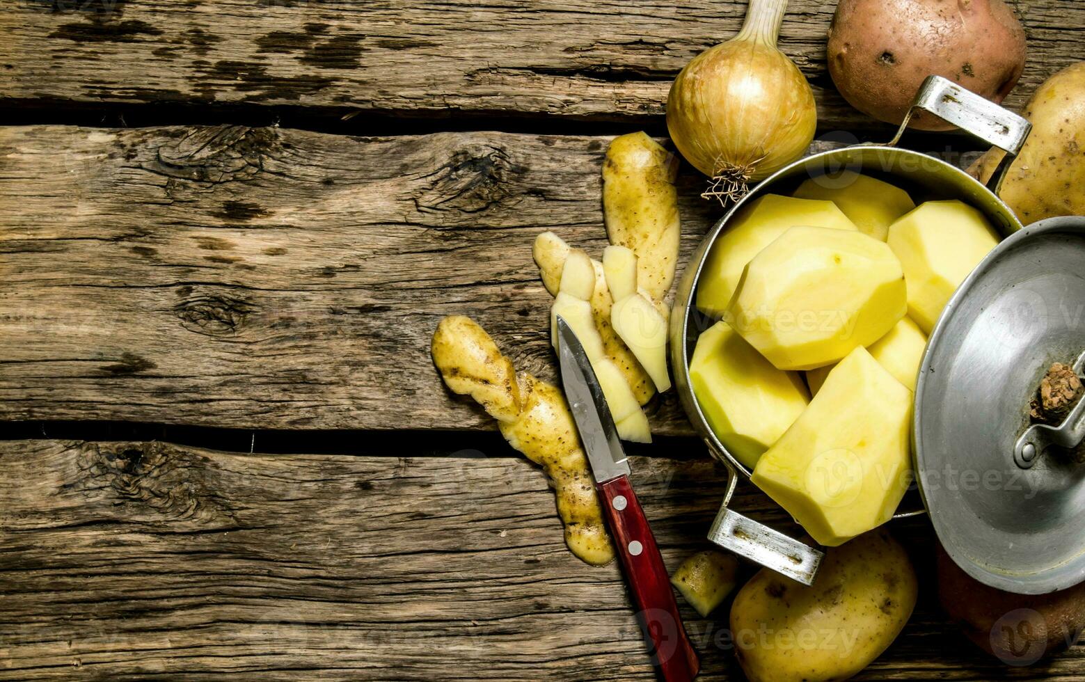 Peeled potatoes in an old pan with knife on wooden table . Free space for text. photo