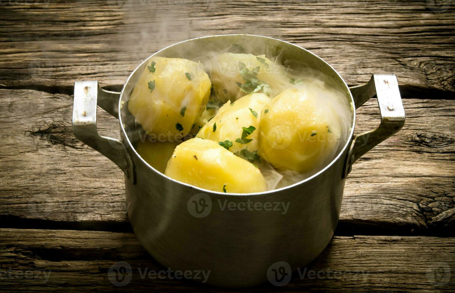Boiled potatoes with herbs and steam on a wooden table . photo