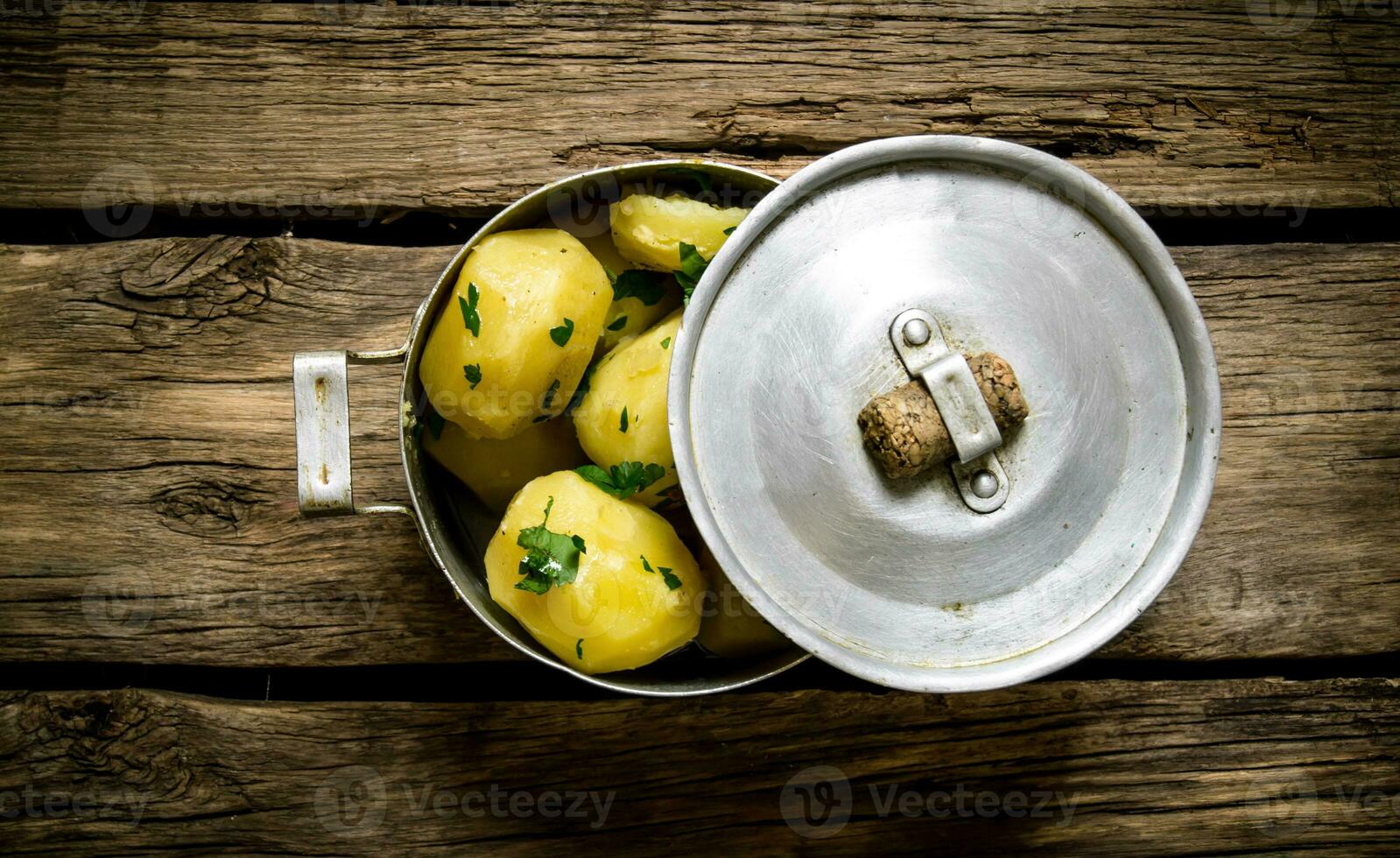Boiled potatoes with herbs in an old pot on a wooden table . photo