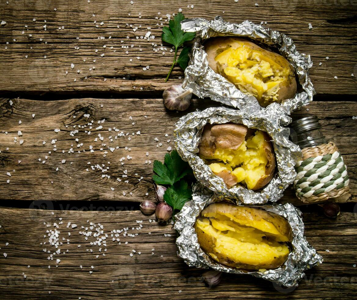 Baked potatoes in foil on a wooden table . Free space for text. photo