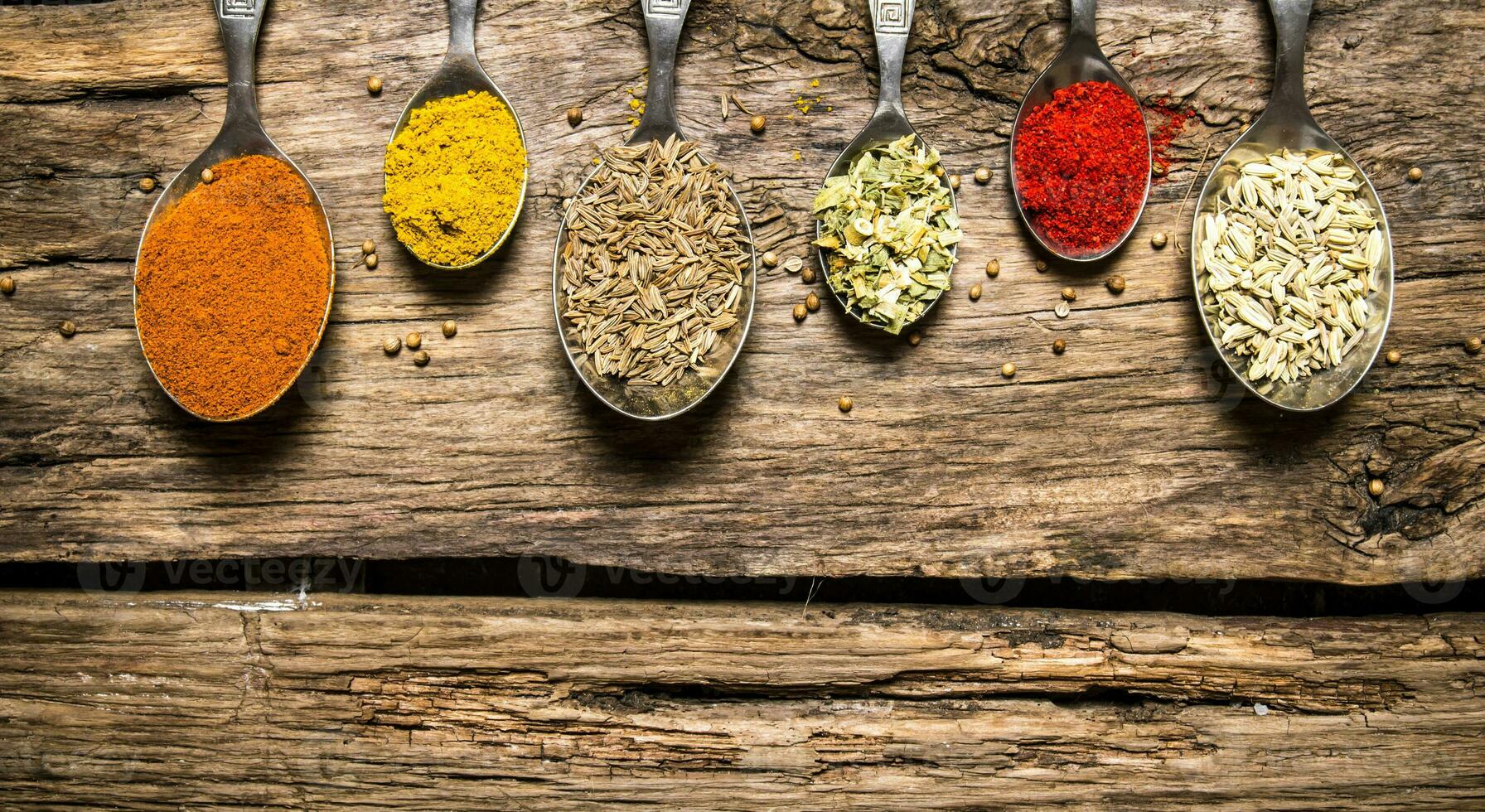 Different kinds of spices in spoons. On wooden background. photo