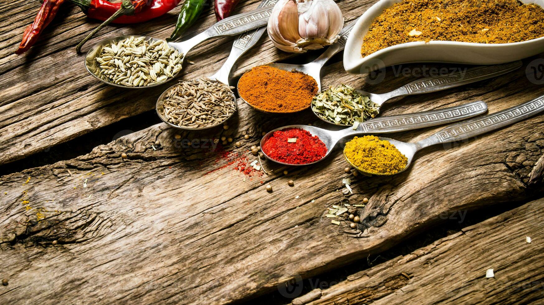 Different kinds of spices in spoons. On wooden background. photo