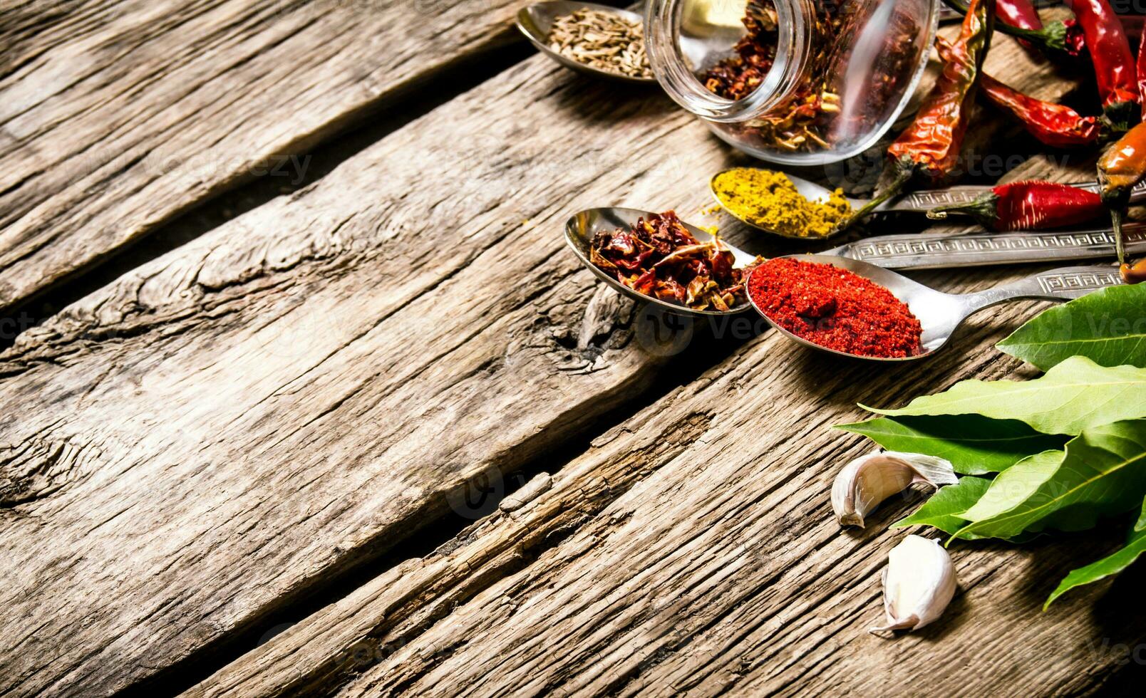 A lot of different spices in spoons with herbs and garlic. photo