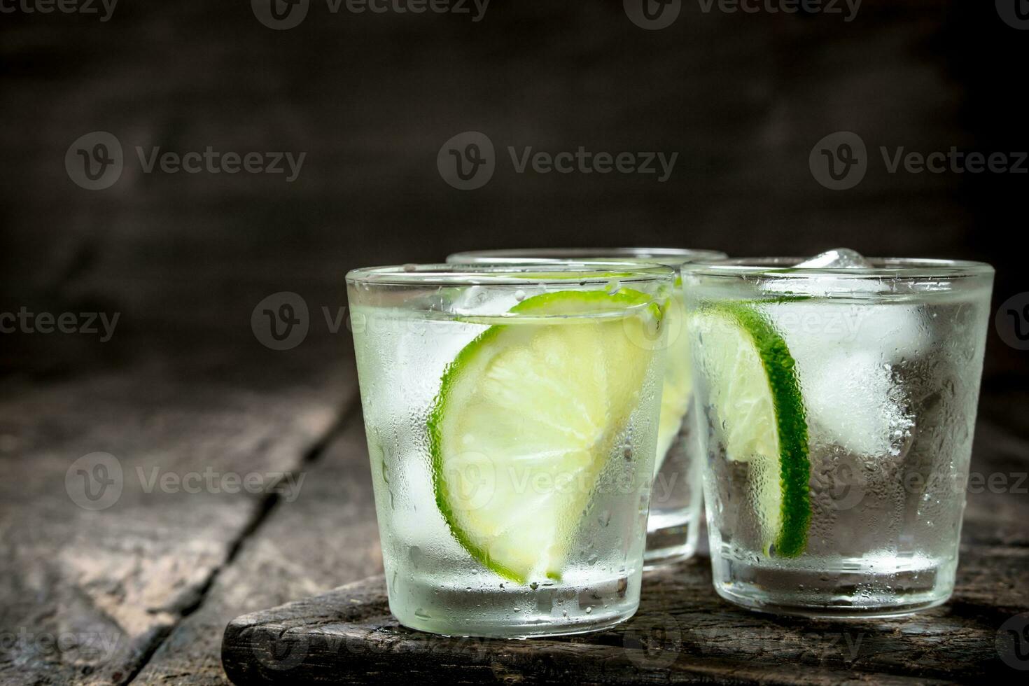 Vodka shots with lime and ice on the board. photo