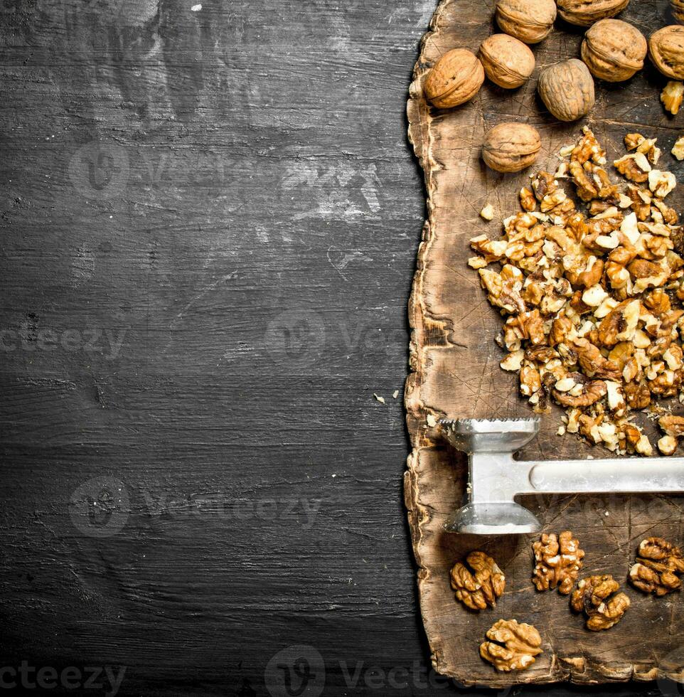 Crushed walnuts with a hammer on the old Board. photo