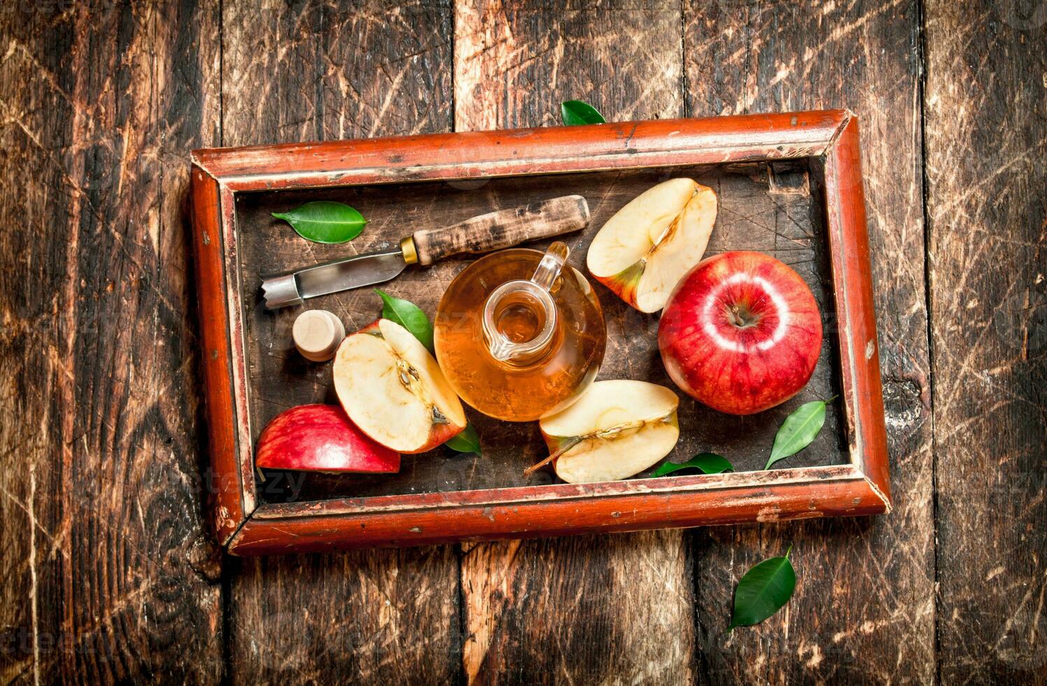 Apple cider vinegar, red apples in the old tray . photo