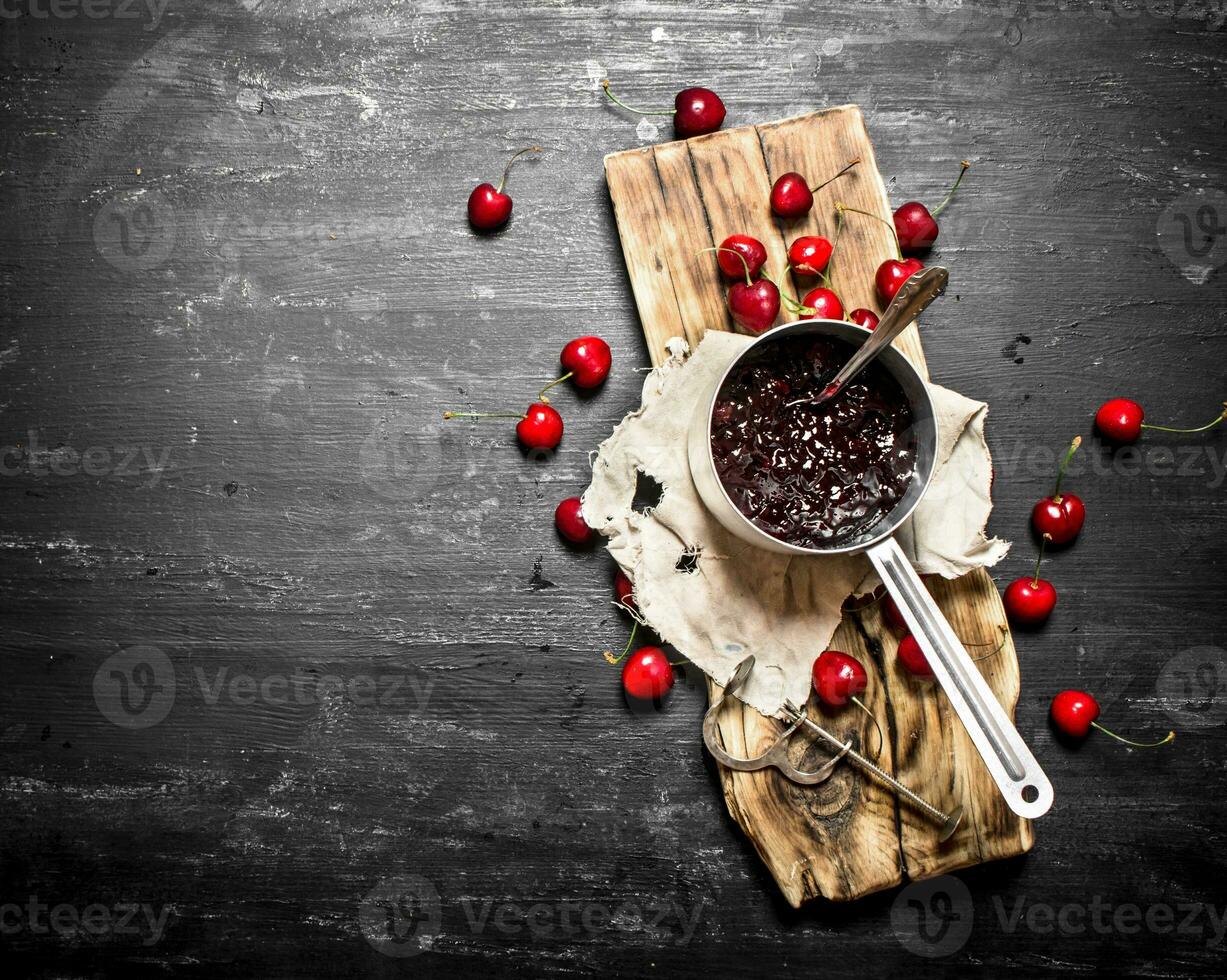 Fresh cherry jam in a saucepan on old Board. photo