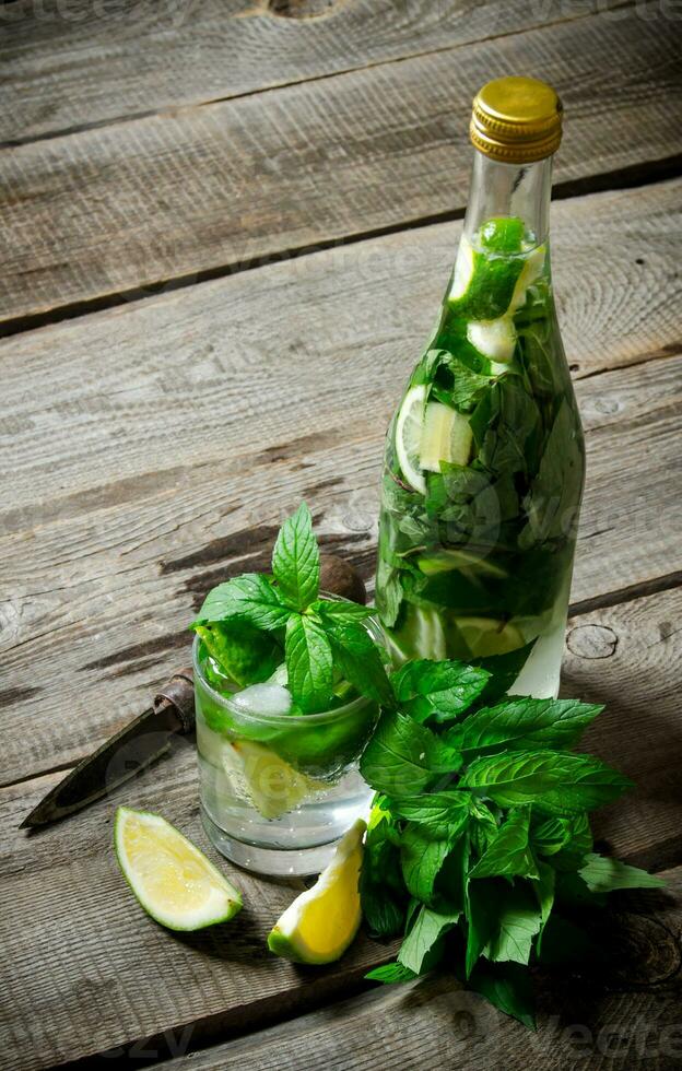 Cocktail in glass and bottle , also mint and limes on a wooden table . photo