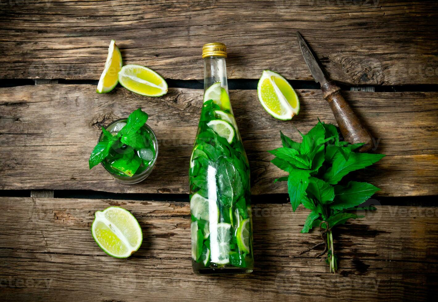 The ingredients for the cocktail - limes, mint, knife, is also prepared cocktail in the bottle and in the glass. photo