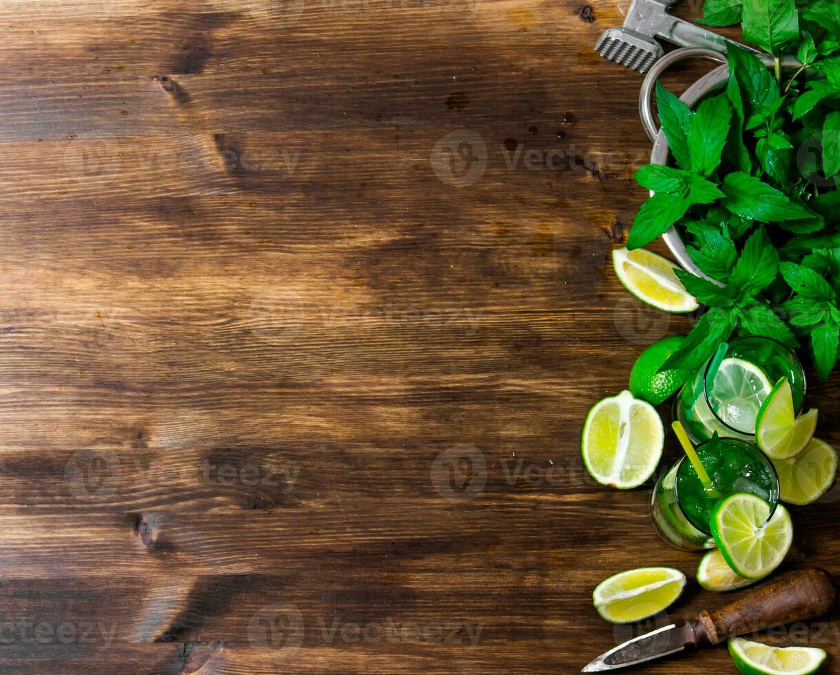 The ingredients for the cocktail - limes, rum, mint leaves, ice cubes on wooden table. Free space for text. photo