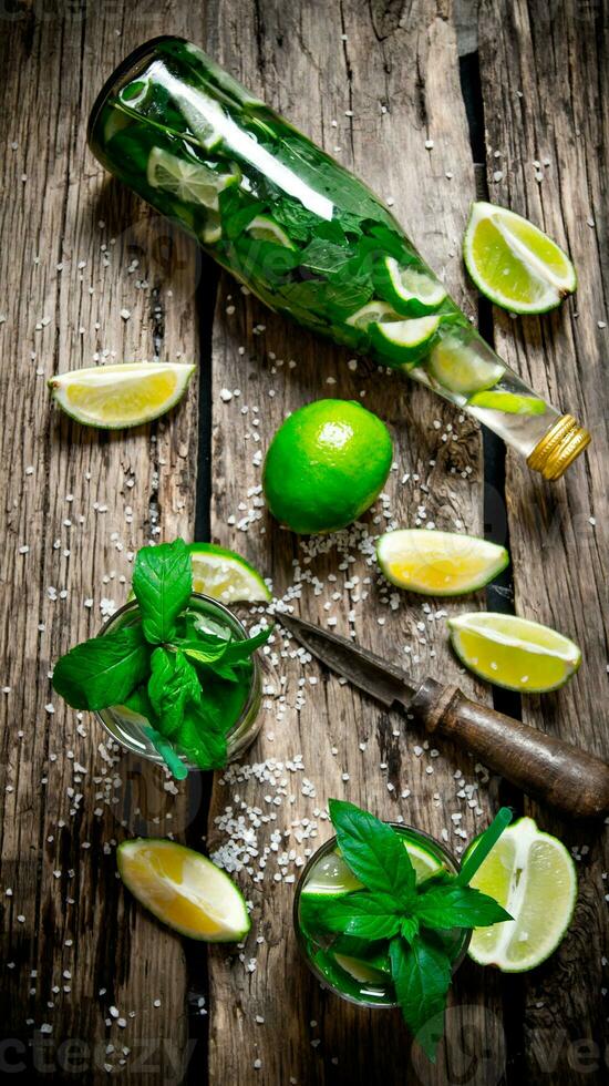 The ingredients for the cocktail - limes, mint, knife, is also prepared cocktail in the bottle and in the glass. photo