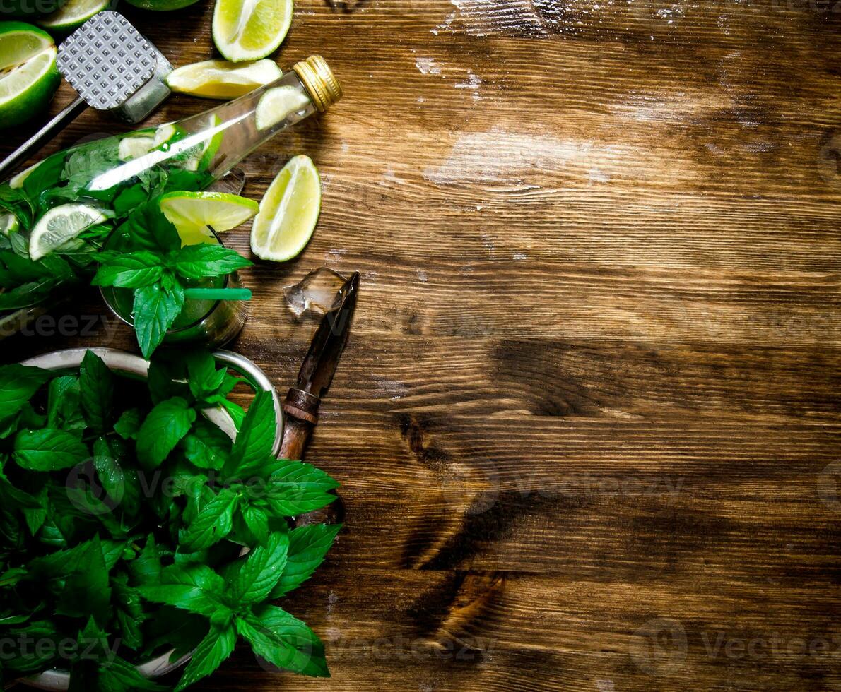The ingredients for the cocktail - limes, rum, mint leaves, ice cubes on wooden table. Free space for text. photo