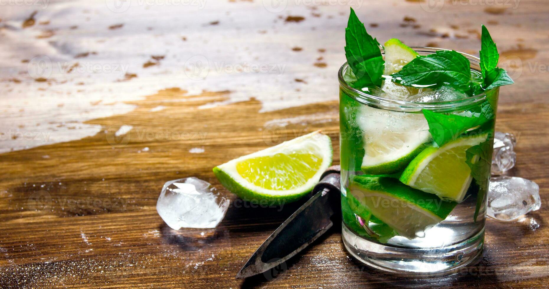Glass of cool cocktail , ice, knife and slices of lime on a wooden table. photo