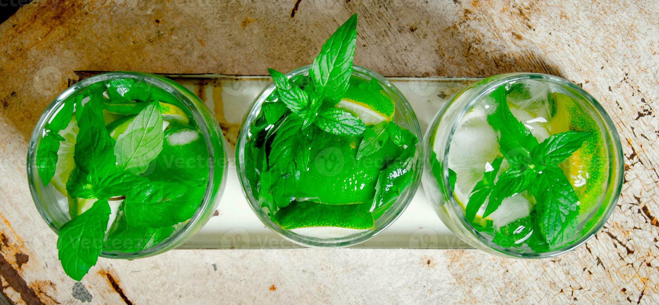 Three cocktail glasses with ice cubes, lime, mint leaves and rum . On the old background. photo