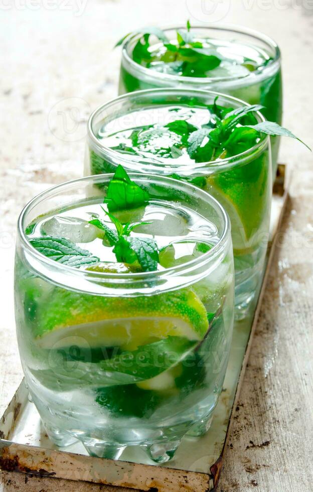 Three cocktail glasses with ice cubes, lime, mint leaves and rum . On the old background. photo