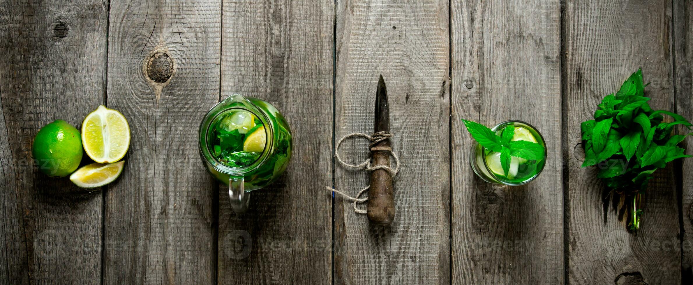 The ingredients for the cocktail - mint leaves, limes, rum and a knife for citrus fruits on the wooden table. photo