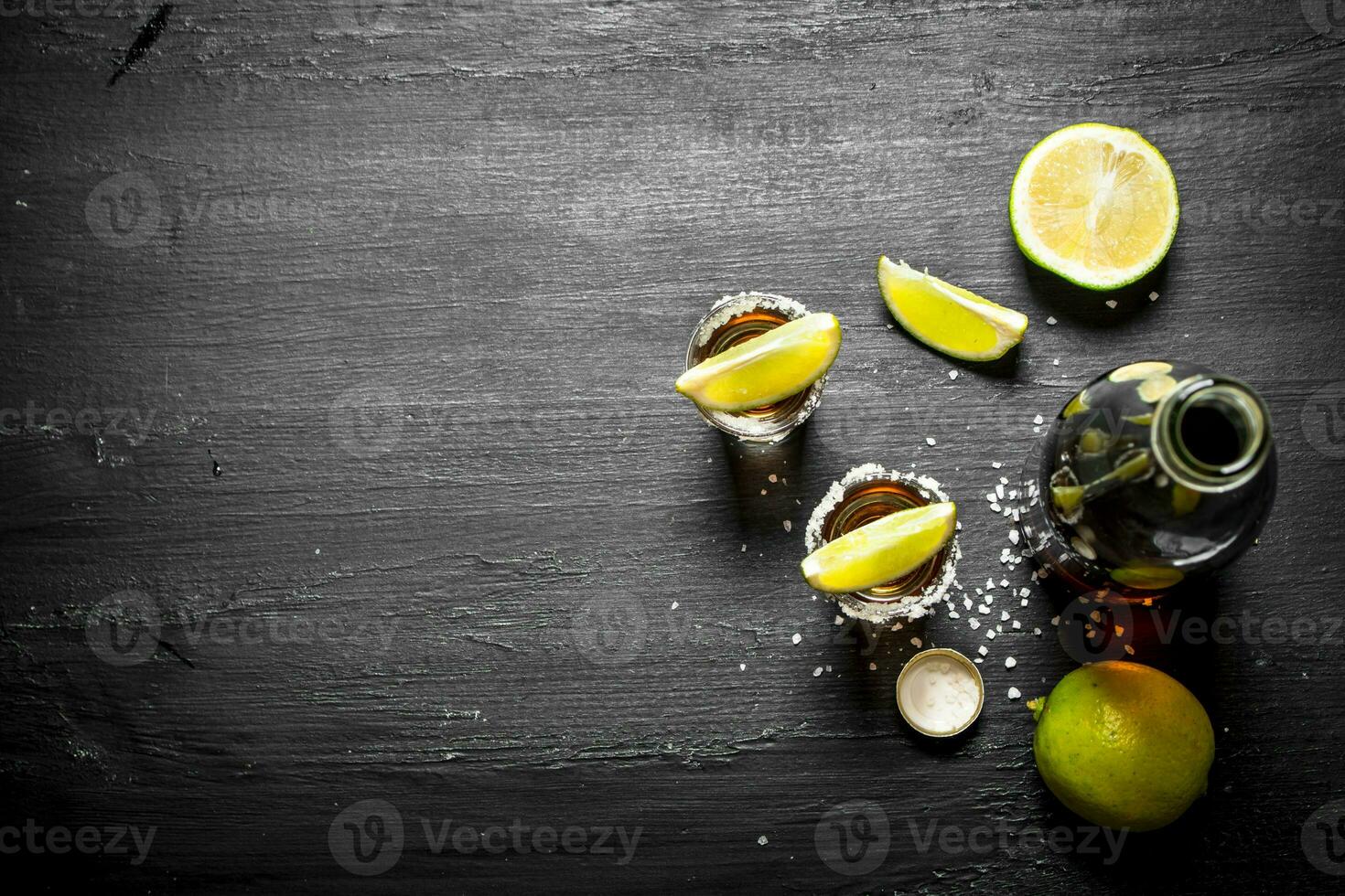 bottle of tequila with shot glasses, fresh lime and salt. photo