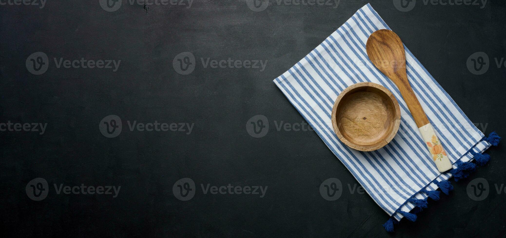 Empty bowl and wooden spoon on a black table, top view. Copy space photo