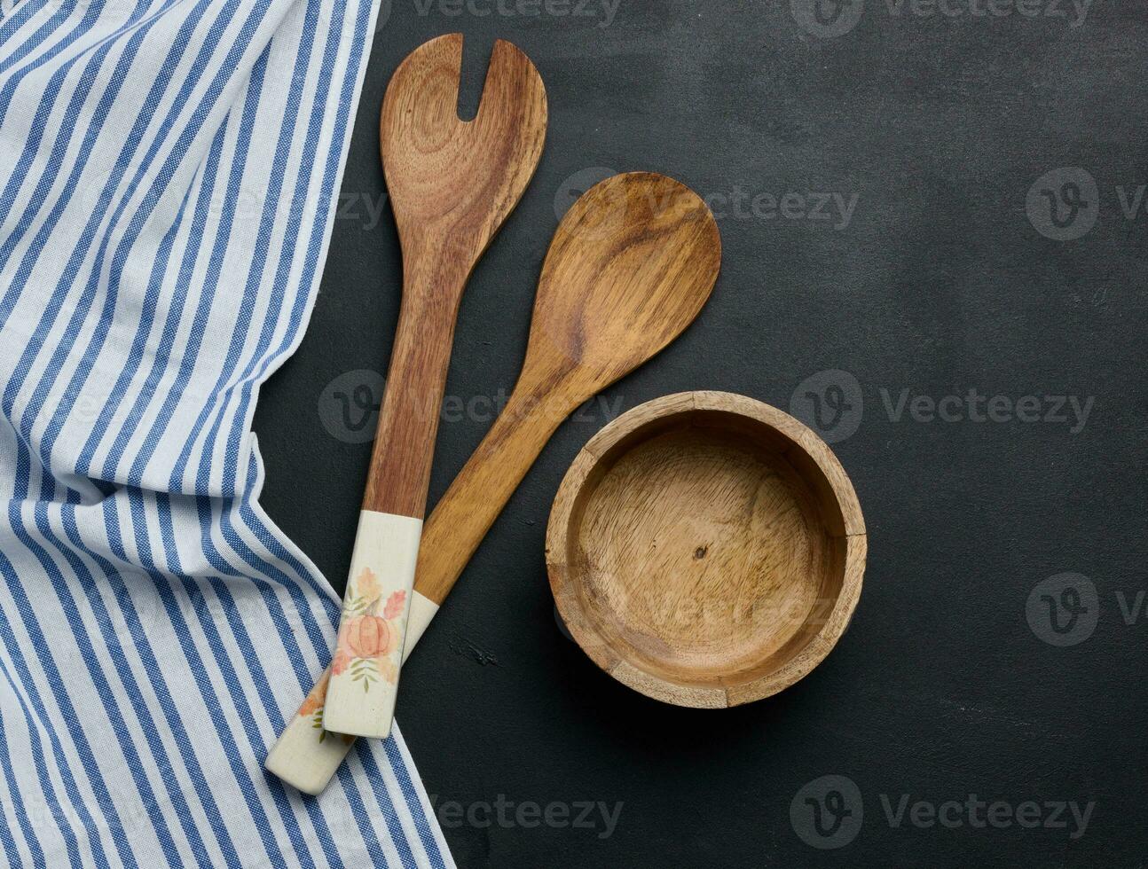 Empty bowl and wooden spoons on a black table, top view photo