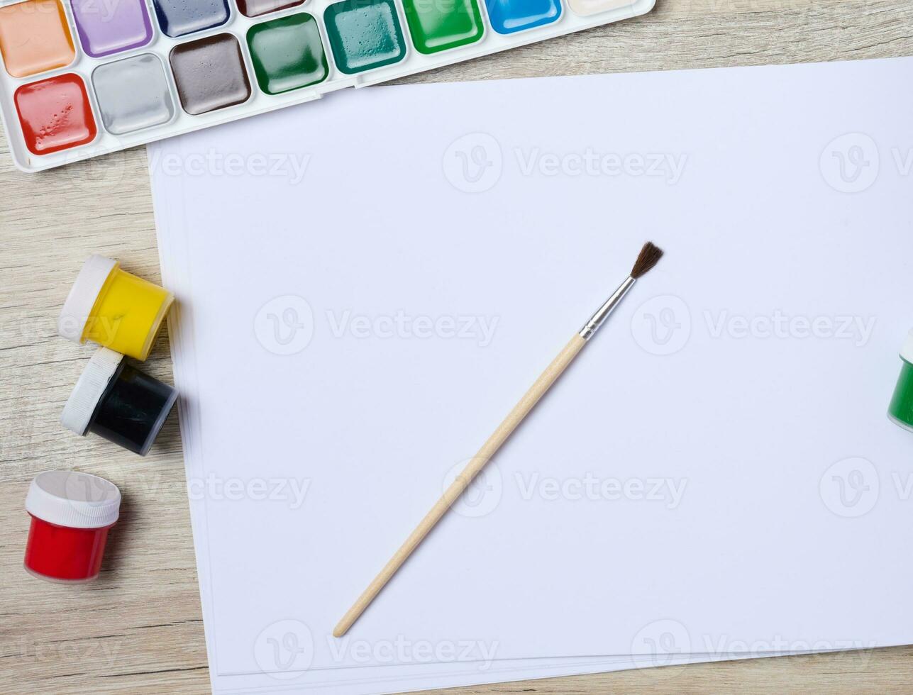 Open sketchbook with blank white sheets and acrylic paints, top view photo