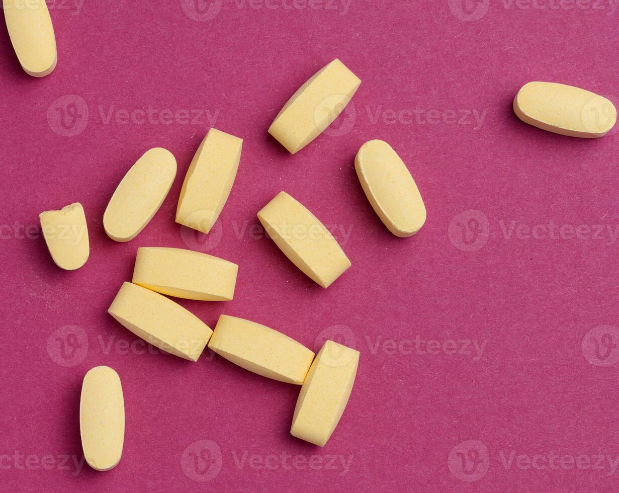 Yellow oval tablets on a pink background, top view photo
