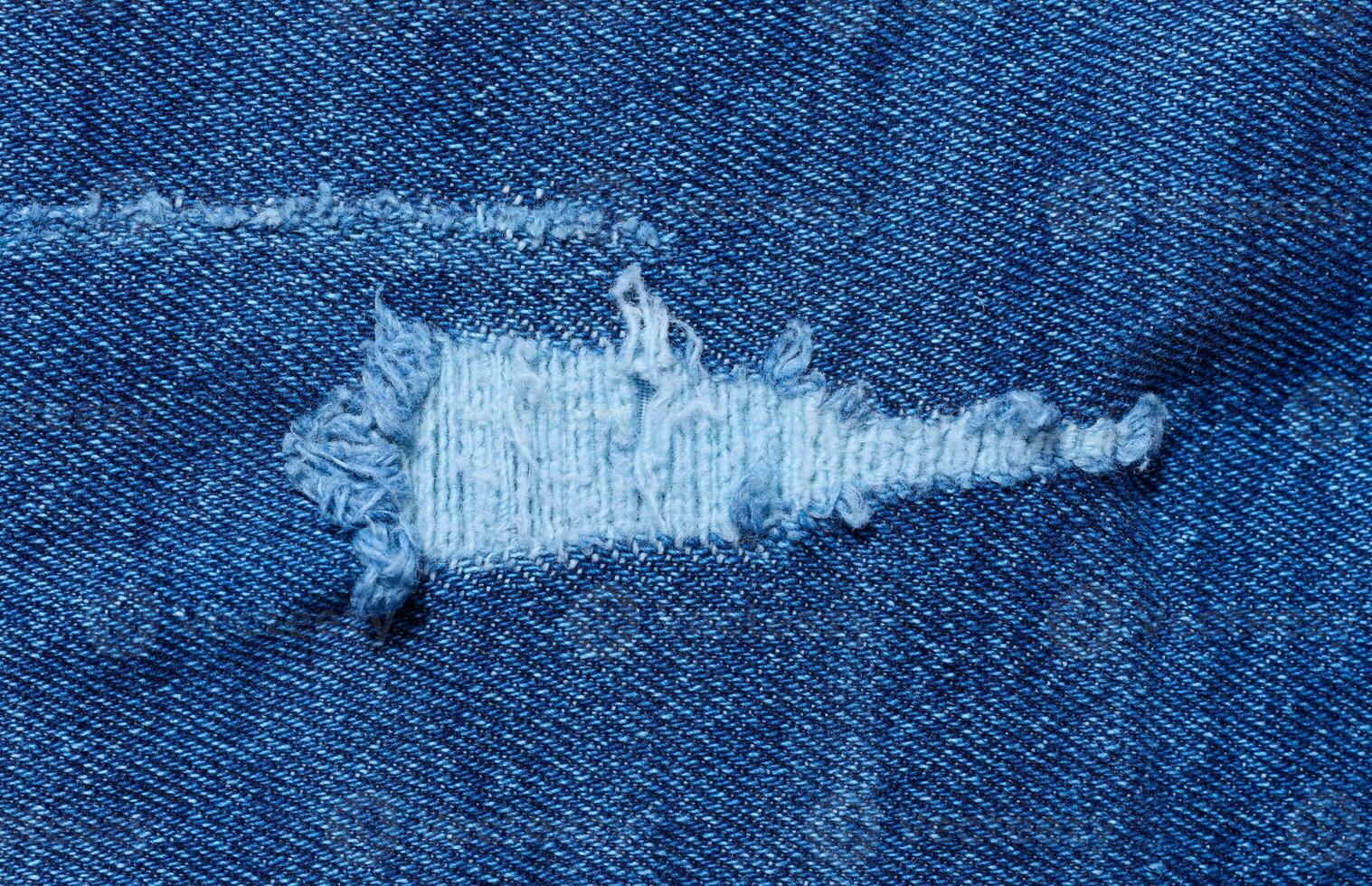 Fragment of blue jeans fabric with a hole, full frame, close up photo