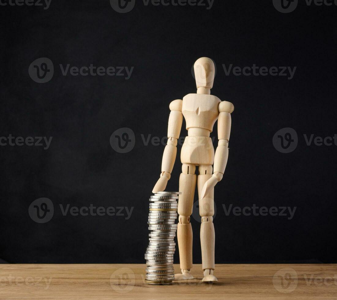 Wooden mannequin and stack of coins on a black background. Business growth concept photo