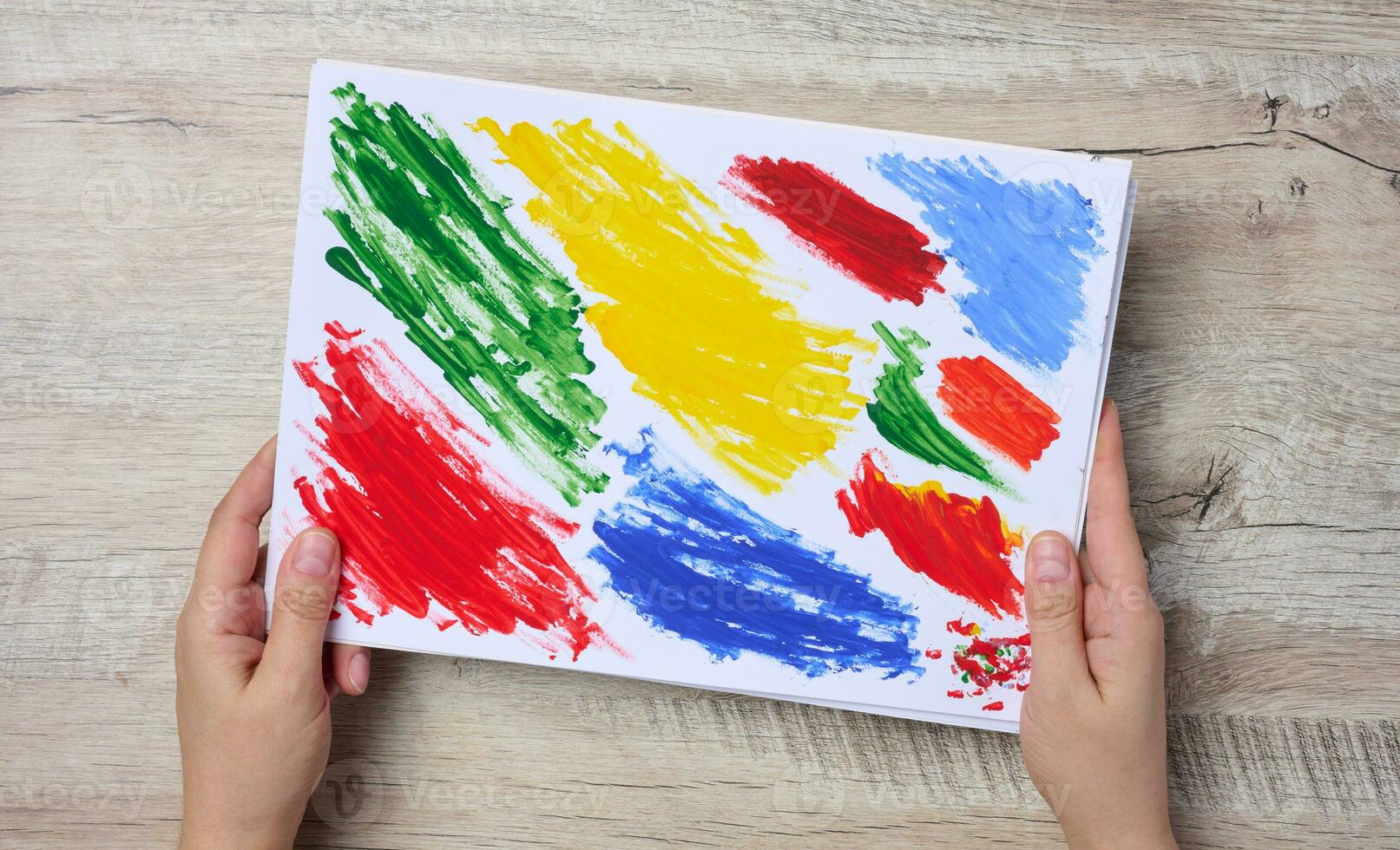 Female hands holding a white sheet of paper with strokes of acrylic multi-colored paint, top view photo