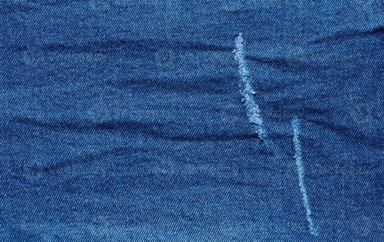 Fragment of blue jeans fabric with a hole, full frame, close up photo