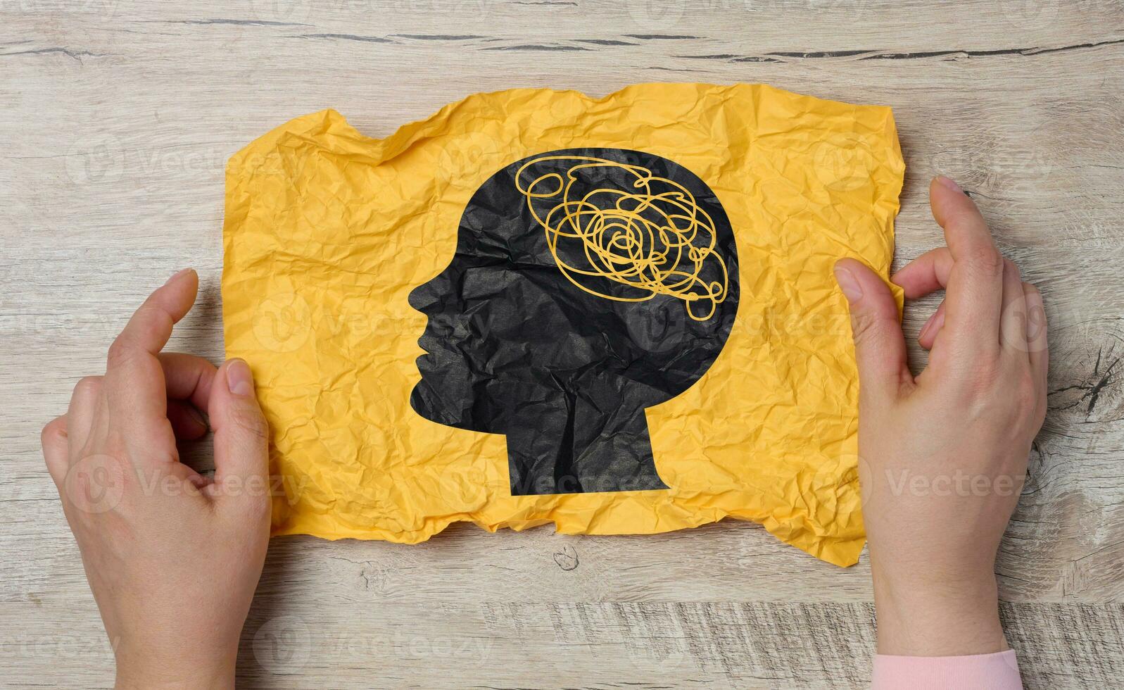 A female hand holds a crumpled paper with a black silhouette of a person's head and tangled threads inside, representing the concept of human mental health photo