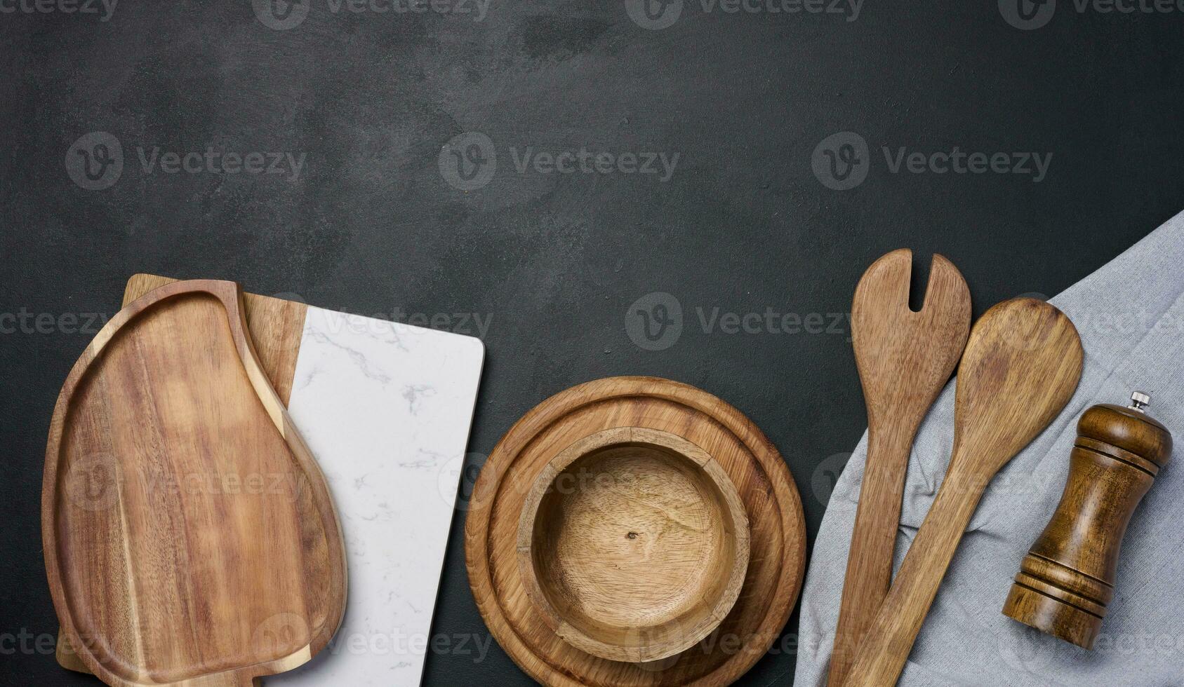 Empty bowl and wooden spoons on a black table, top view photo