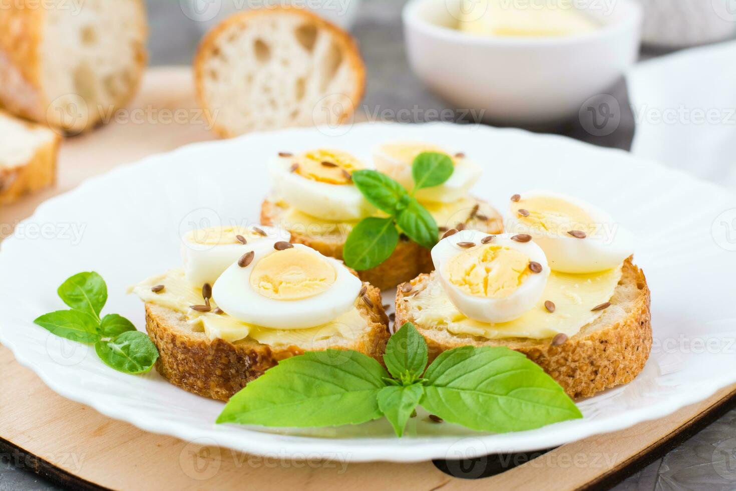 Hearty breakfast in the morning. Fresh baguette sandwiches with butter, quail eggs, flax seeds and basil seeds on a plate. Close-up photo
